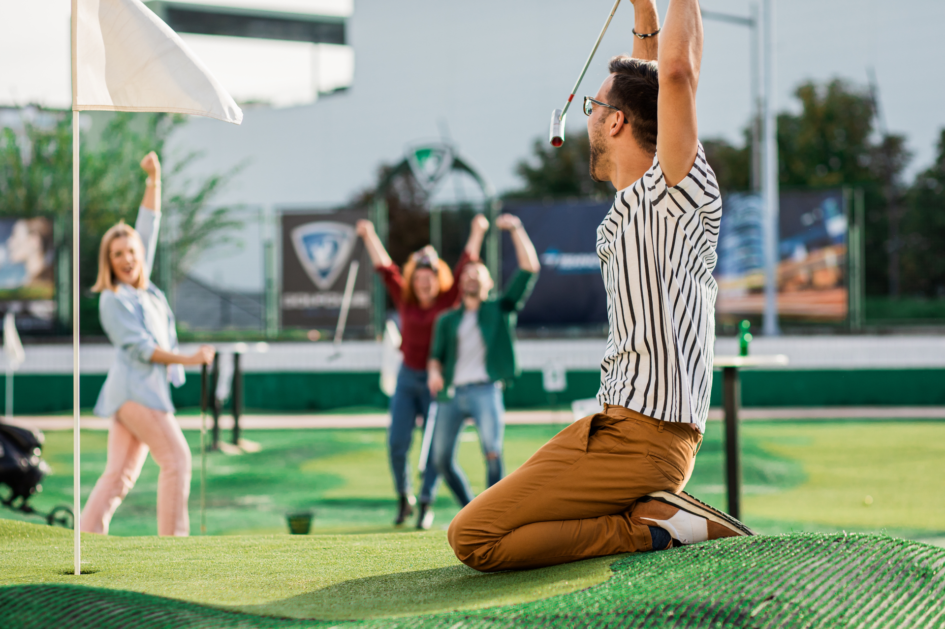 A man celebrating a putt on his knees while his friends cheer behind him