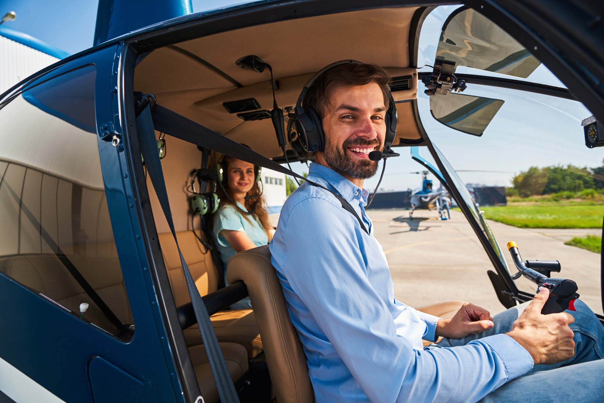 A smiling pilot and passenger seated in a helicopter before take-off