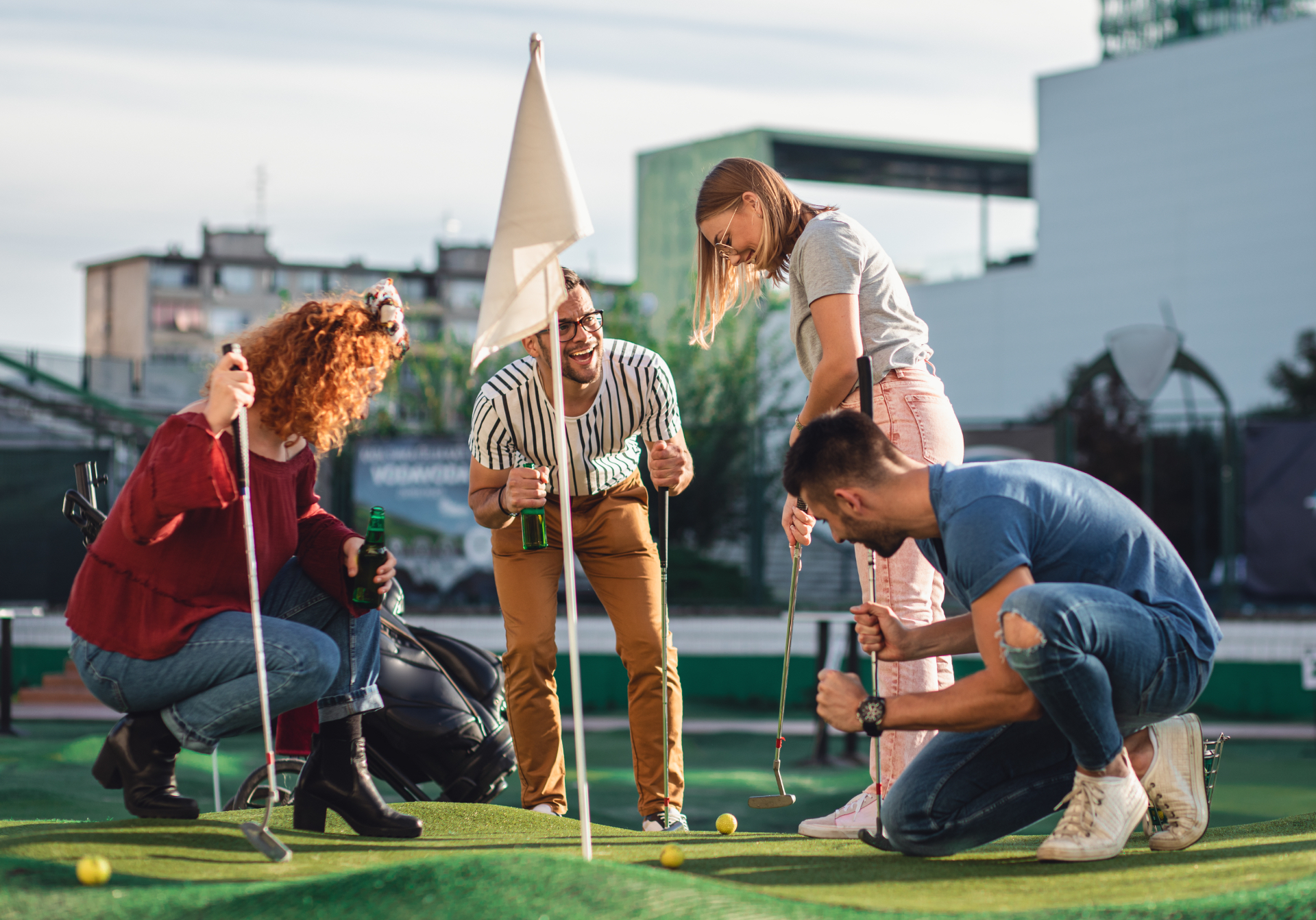 Four friends laughing around the hole on a crazy golf course at sunset